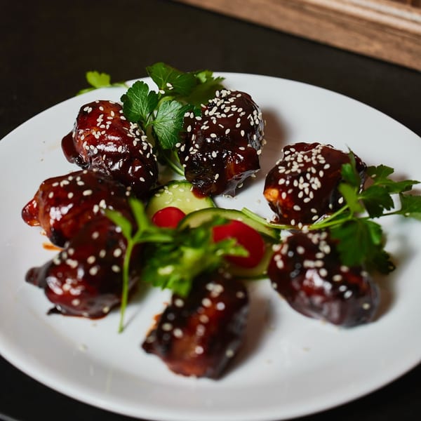 Glazed chicken wings with sesame seeds, parsley, and cucumber slices on a white plate.