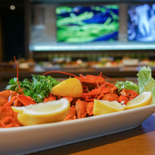 A white platter of red crawfish, garnished with lemon wedges, parsley, and lettuce.