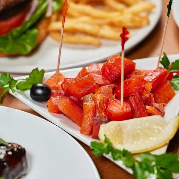 Close-up of a white rectangular plate filled with red diced watermelon, garnished with a lemon wedge and parsley.