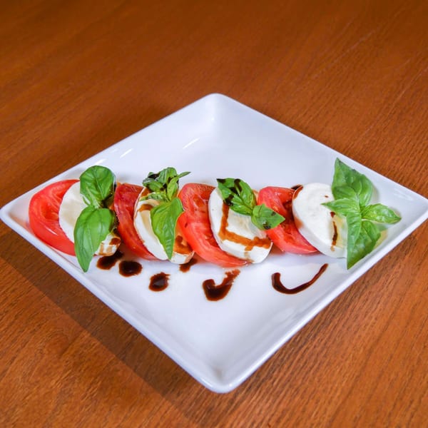 Caprese salad with sliced tomatoes, mozzarella, fresh basil, and balsamic glaze on a white plate.
